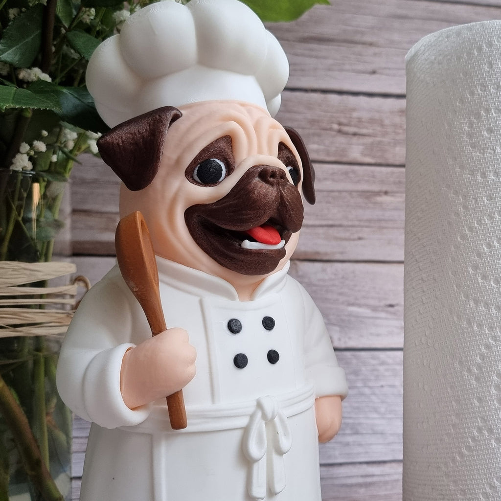 The pug chef next to a loaded paper towel roll on a kitchen shelf