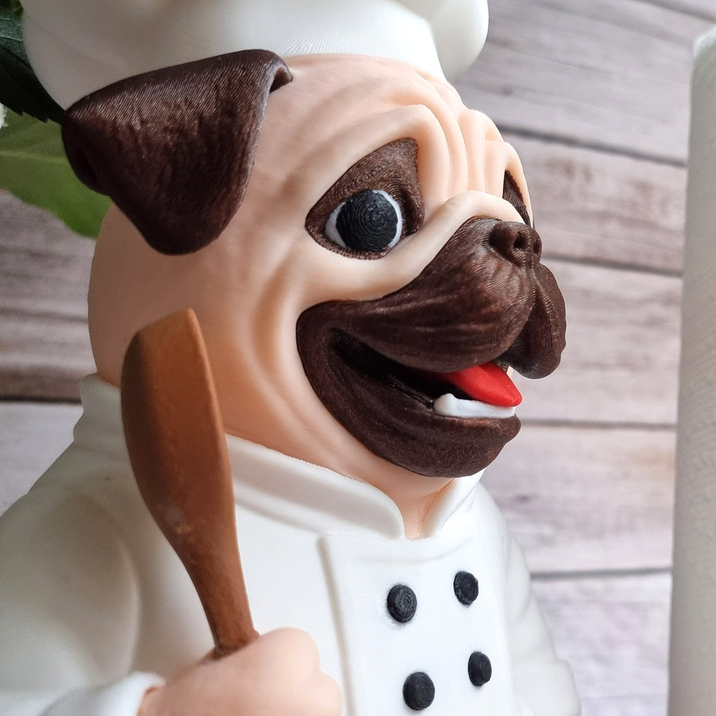 Close-up of the pug's face: dark mask, black eyes, red tongue and the chef's hat